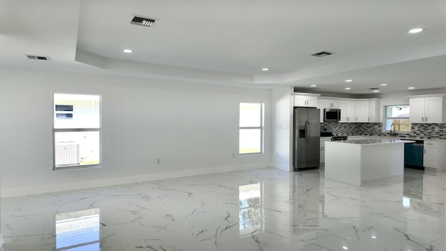 kitchen with a raised ceiling, white cabinetry, a kitchen island, and stainless steel appliances