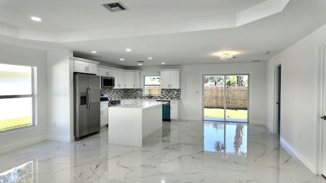 kitchen with decorative backsplash, stainless steel appliances, sink, a center island, and white cabinetry