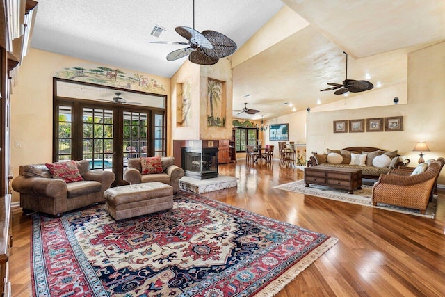 living room with a wood stove, high vaulted ceiling, french doors, a textured ceiling, and wood-type flooring