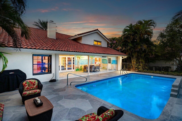 pool at dusk with grilling area, french doors, and a patio