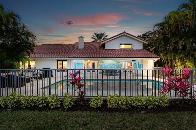 back house at dusk featuring a patio area and a fenced in pool