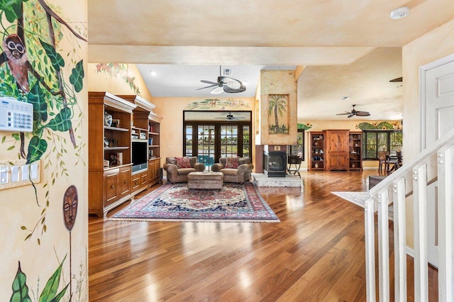 living room featuring wood-type flooring, lofted ceiling with beams, a wood stove, and ceiling fan