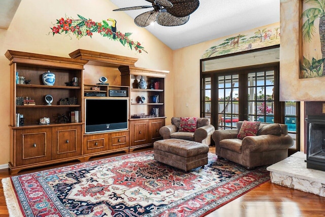 living room featuring hardwood / wood-style flooring, a stone fireplace, ceiling fan, and lofted ceiling