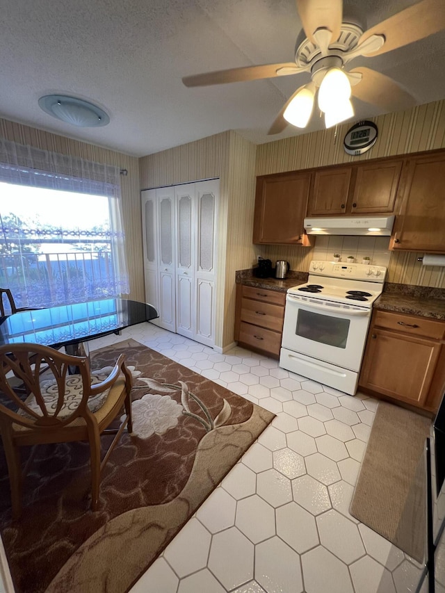 kitchen featuring under cabinet range hood, light tile patterned floors, brown cabinetry, white range with electric cooktop, and dark countertops