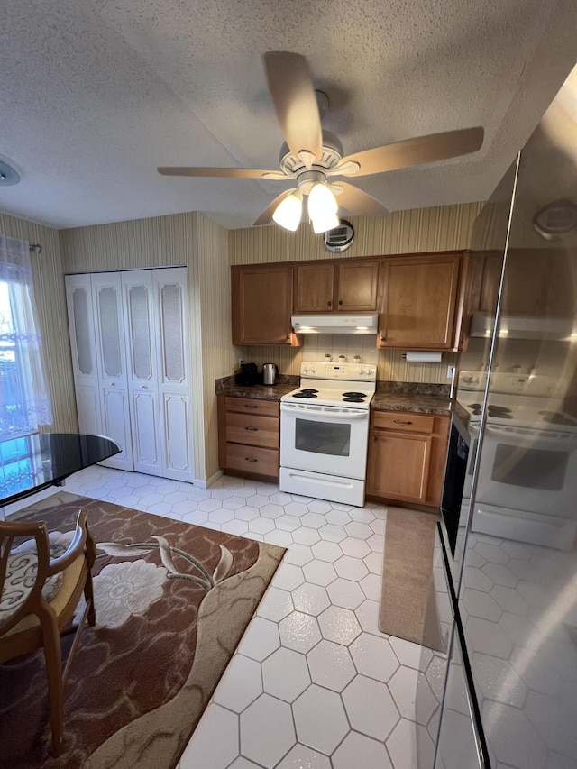 kitchen featuring a textured ceiling, brown cabinets, white range with electric stovetop, dark countertops, and a ceiling fan
