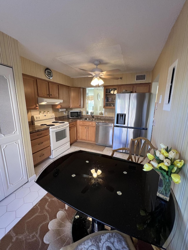 kitchen with stainless steel appliances, light tile patterned floors, under cabinet range hood, a sink, and visible vents