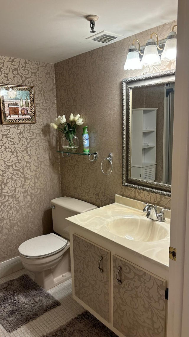 bathroom with vanity, toilet, visible vents, baseboards, and wallpapered walls