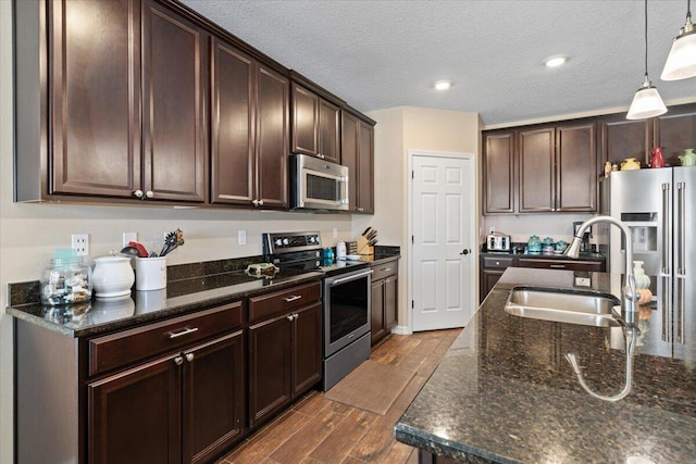 kitchen featuring pendant lighting, sink, dark stone countertops, dark brown cabinetry, and stainless steel appliances