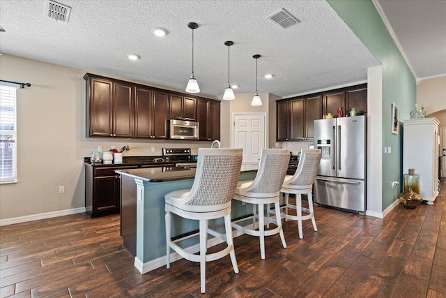 kitchen featuring pendant lighting, crown molding, an island with sink, appliances with stainless steel finishes, and dark brown cabinets