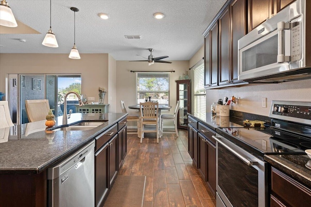 kitchen featuring dark brown cabinetry, sink, hanging light fixtures, stainless steel appliances, and a kitchen island with sink