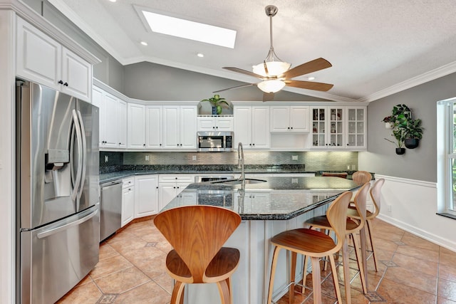 kitchen featuring stainless steel appliances, tasteful backsplash, dark stone countertops, lofted ceiling with skylight, and white cabinets