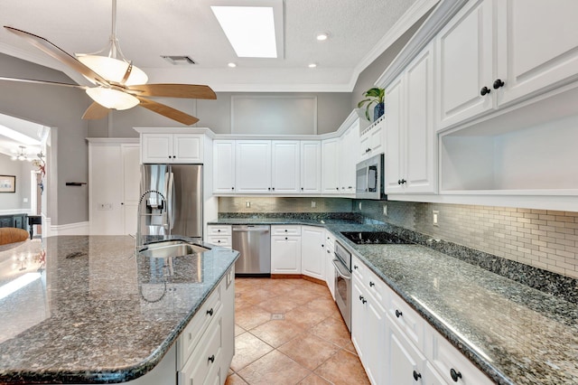 kitchen with a skylight, ceiling fan, dark stone countertops, white cabinetry, and stainless steel appliances