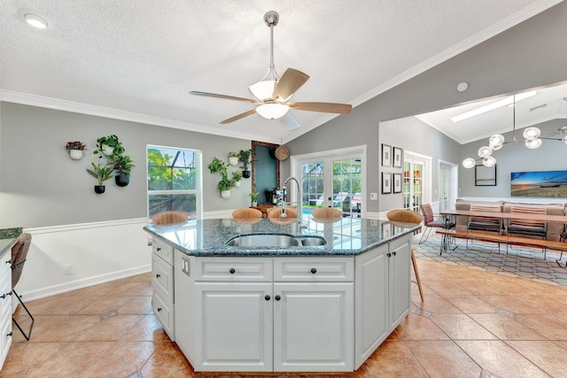 kitchen with vaulted ceiling with skylight, ceiling fan, sink, white cabinets, and an island with sink