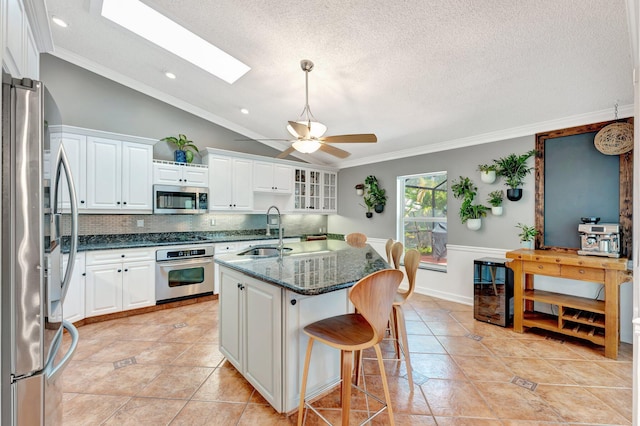 kitchen with white cabinets, vaulted ceiling with skylight, stainless steel appliances, and sink