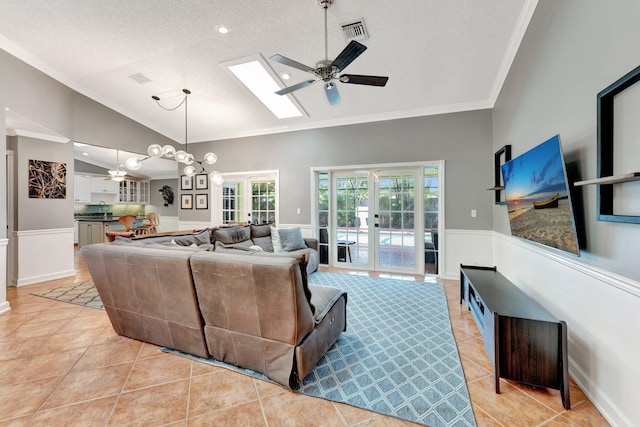 tiled living room featuring french doors, a textured ceiling, lofted ceiling with skylight, and ceiling fan