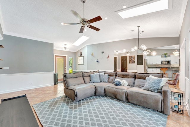 living room featuring ceiling fan, light tile patterned flooring, lofted ceiling with skylight, and ornamental molding