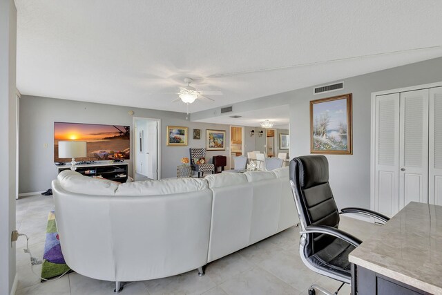 living room with ceiling fan, light tile patterned flooring, and a textured ceiling