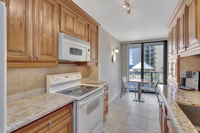 kitchen featuring decorative backsplash, light stone counters, light tile patterned floors, and white appliances