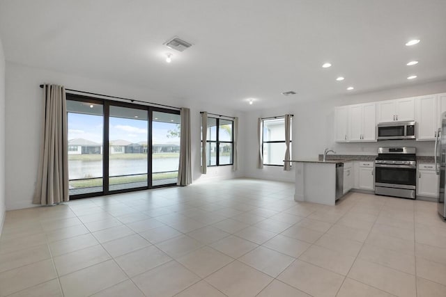 kitchen with stainless steel appliances, light tile patterned floors, kitchen peninsula, a water view, and white cabinets