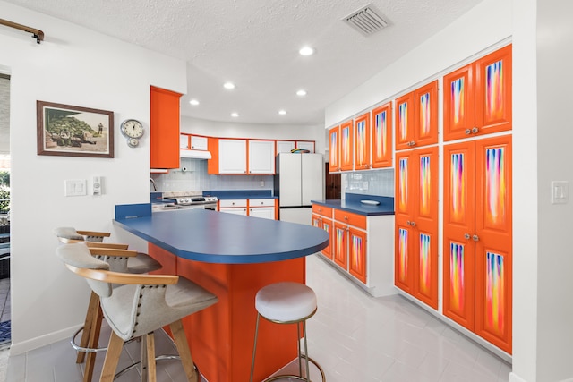 kitchen featuring a kitchen breakfast bar, light tile patterned floors, a textured ceiling, tasteful backsplash, and white fridge