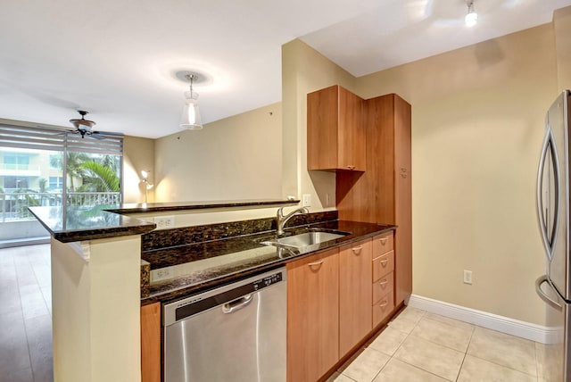 kitchen with kitchen peninsula, appliances with stainless steel finishes, dark stone counters, sink, and hanging light fixtures