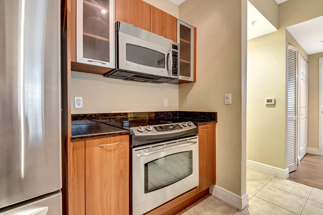 700 E Boynton Beach Blvd Unit 407, Boynton Beach, FL 33435 - kitchen with appliances with stainless steel finishes, light tile patterned flooring, dark stone countertops, and glass insert cabinets