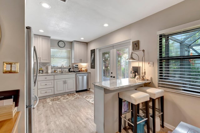 kitchen with light stone countertops, light wood-type flooring, tasteful backsplash, a kitchen bar, and stainless steel appliances