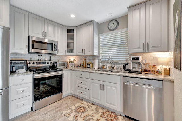 kitchen with sink, decorative backsplash, appliances with stainless steel finishes, light hardwood / wood-style floors, and light stone counters