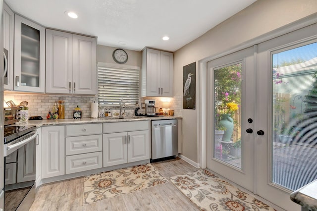 kitchen featuring dishwasher, sink, electric range, light wood-type flooring, and light stone countertops