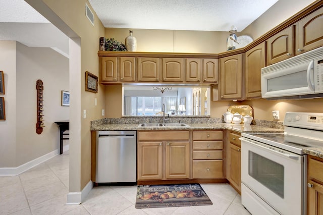 kitchen with sink, light stone counters, a textured ceiling, white appliances, and light tile patterned flooring