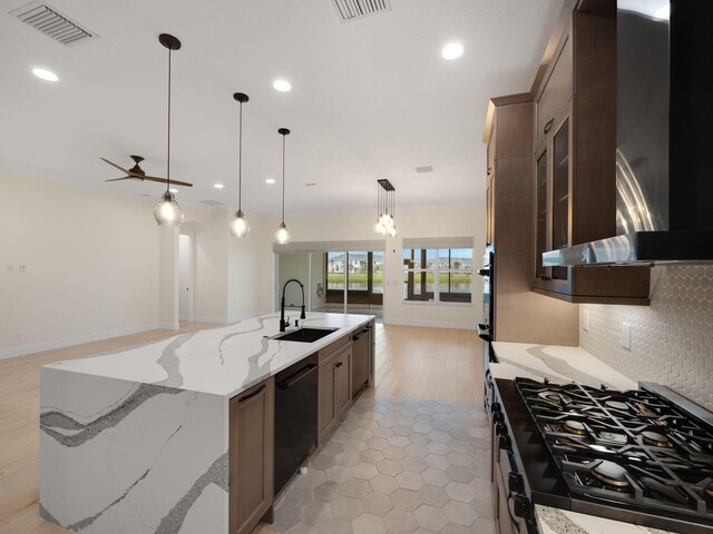 kitchen featuring black appliances, a spacious island, wall chimney exhaust hood, light stone countertops, and decorative light fixtures