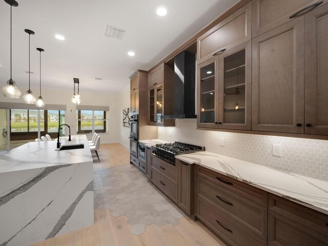 kitchen with appliances with stainless steel finishes, backsplash, light stone counters, wall chimney exhaust hood, and hanging light fixtures