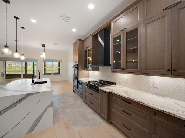 kitchen with backsplash, wall chimney exhaust hood, light stone countertops, decorative light fixtures, and stainless steel gas cooktop