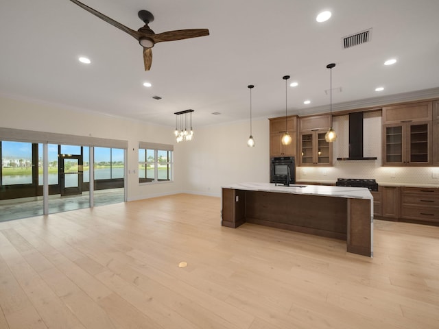 kitchen featuring ceiling fan, wall chimney exhaust hood, pendant lighting, and ornamental molding