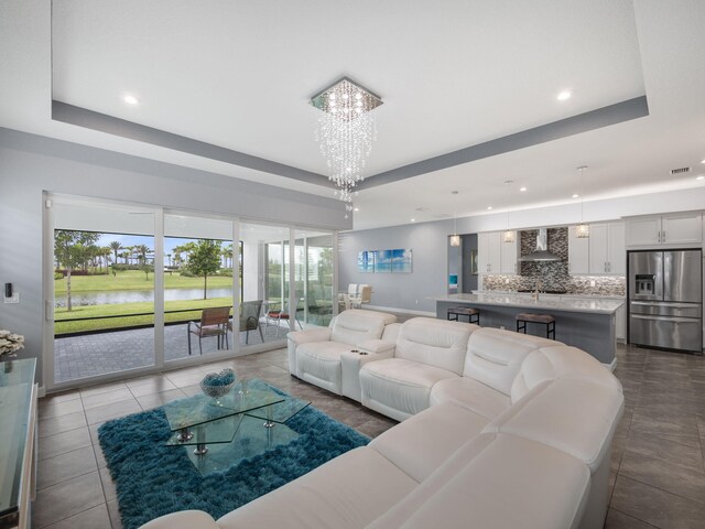 tiled living room featuring a raised ceiling, a water view, and an inviting chandelier