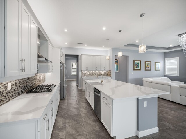 kitchen with a large island with sink, stainless steel appliances, white cabinetry, and hanging light fixtures