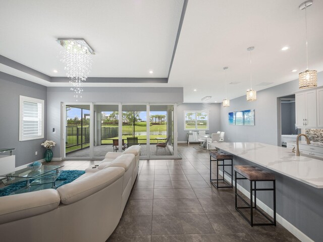 living room featuring a raised ceiling, a notable chandelier, and sink