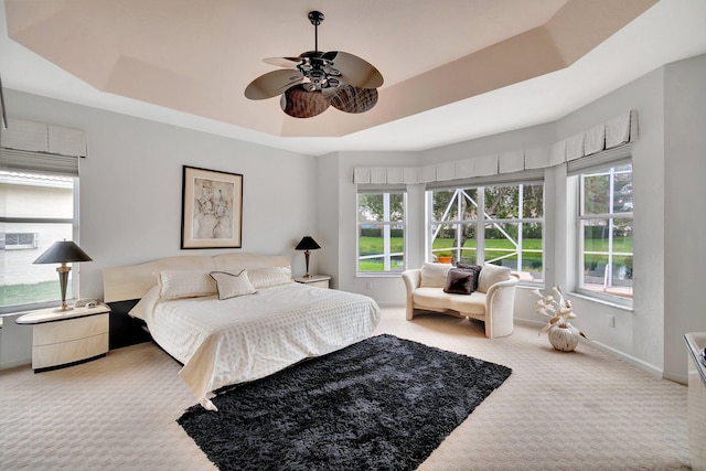 carpeted bedroom with a raised ceiling, multiple windows, and ceiling fan