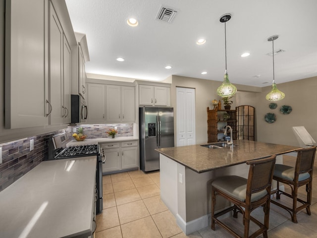 kitchen featuring pendant lighting, a kitchen island with sink, sink, decorative backsplash, and appliances with stainless steel finishes