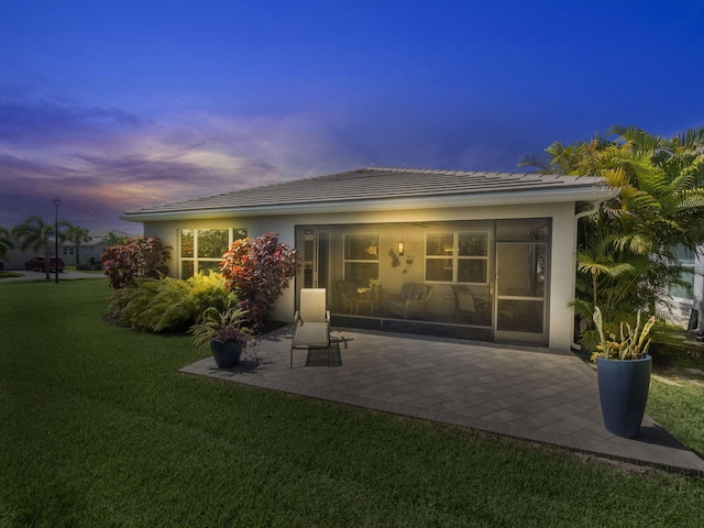 back house at dusk featuring a patio area and a yard