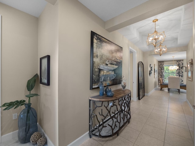 corridor with a tray ceiling, light tile patterned floors, and a notable chandelier