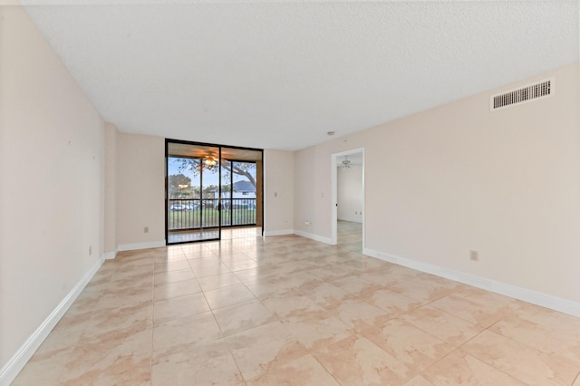 unfurnished room with a textured ceiling, expansive windows, and ceiling fan