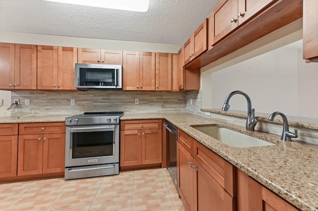 kitchen with sink, light stone counters, a textured ceiling, light tile patterned floors, and appliances with stainless steel finishes