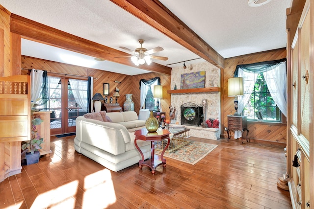 living room featuring ceiling fan, a fireplace, beam ceiling, wooden walls, and a textured ceiling