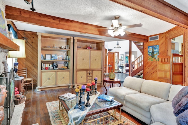 living room with wood walls, ceiling fan, dark hardwood / wood-style floors, a textured ceiling, and beam ceiling