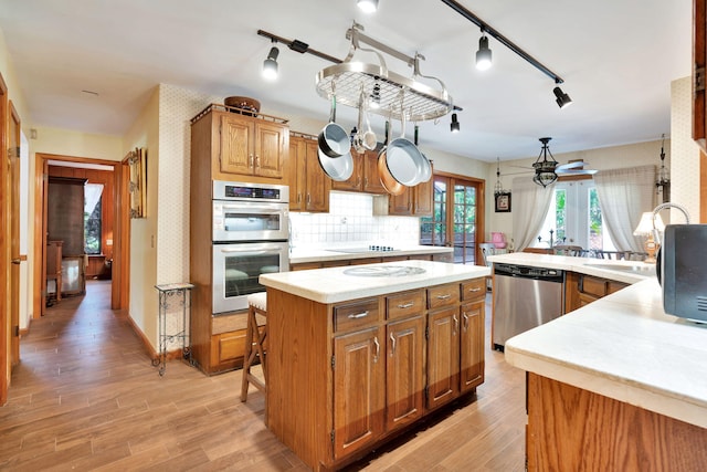 kitchen featuring appliances with stainless steel finishes, a kitchen island, backsplash, ceiling fan, and light hardwood / wood-style flooring