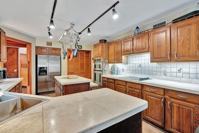 kitchen featuring stainless steel appliances, backsplash, track lighting, a kitchen island, and sink