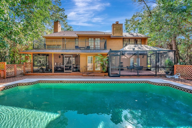 rear view of property with a patio, a chimney, glass enclosure, a balcony, and an outdoor pool