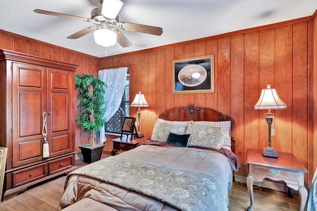 bedroom with a textured ceiling, ceiling fan, light hardwood / wood-style flooring, and wood walls