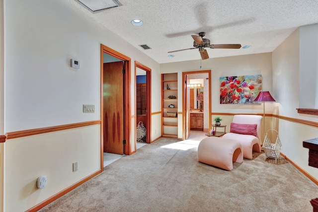 living area with ceiling fan, light colored carpet, a textured ceiling, and built in features